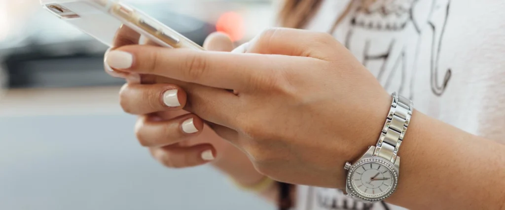 Nell'immagine le mani di una ragazza reggono uno smartphone e con le dita digita sullo schermo.