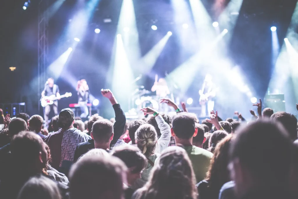 Nell'immagine una folla di persone guarda verso un palco dove una band si sta esibendo